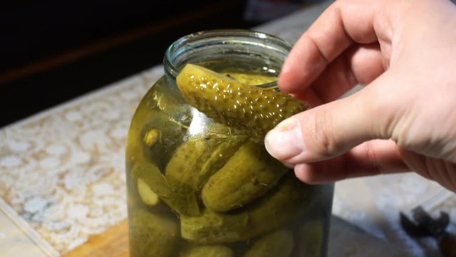 hand get and showing green cucumber from glass jar
