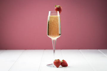 champagne sparkling white wine glass and bottle on plain background with strawberry garnish gold ribbon © Peter