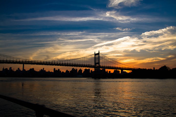 Fototapeta na wymiar Triborough bridge, fence and city with cloudy sunset sky, New York