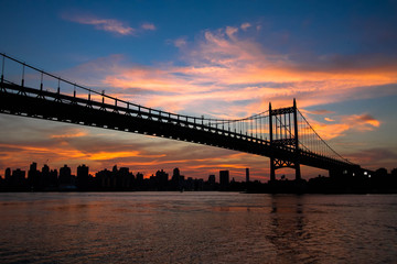 Triborough bridge over the river and buildings in silhouette and sunset sky