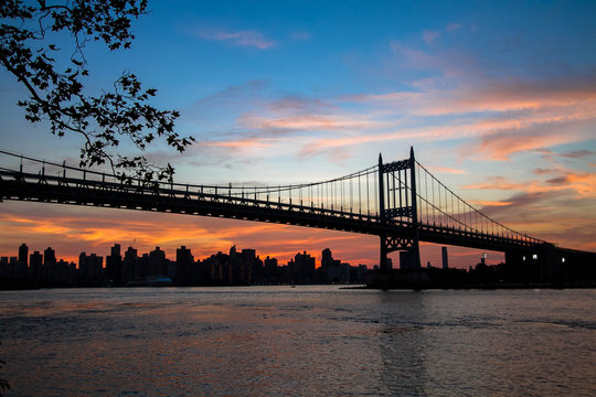 Triborough bridge over the river and buildings in silhouette and sunset sky