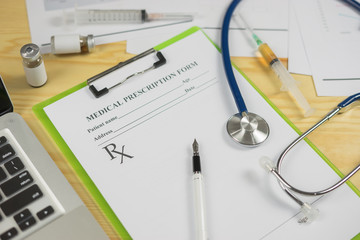 Top view of modern, sterile doctors office desk. Medical accessories,stethoscope laptop pen syring and vaccineprescription with copy space around products.clip board, glasses and other things