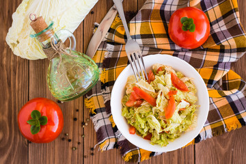Овощной салат, помидоры, пекинская капуста и бутылка с маслом на деревянном столе