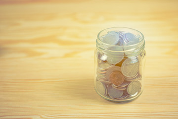 Money and banking concept with coins and glass Jar for savings on wooden background with filter effect retro vintage style