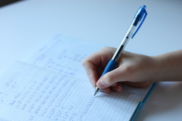 Child's hand writes maths task in notebook
