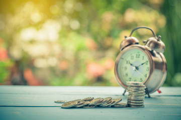 coin stack on wood with alarm clock