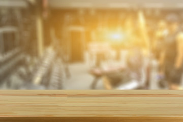 Empty brown wooden table top on blurred background of fitness gym,Young People group of women and men doing sport,interior of new modern club with equipment