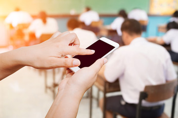 Woman hand hold and touch screen smart phone on blurry background of student assignment in classroom