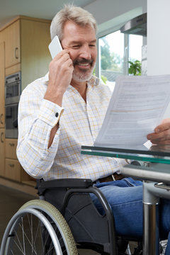 Man In Wheelchair Making Phone Call Whilst Reading Letter
