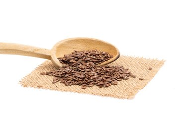 Linseed and a wooden spoon from the left on a piece of sack cloth with white background