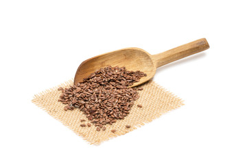 Linseed and a slanted wooden spoon on a piece of sack cloth with white background