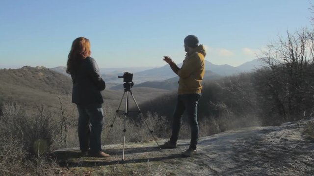 Man and woman make a shot of landscape with camera on the tripod