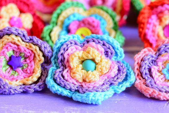 Bright crochet flowers on purple wooden background. Flowers crocheted from colorful cotton yarn. Simple summer handmade DIY idea. Closeup