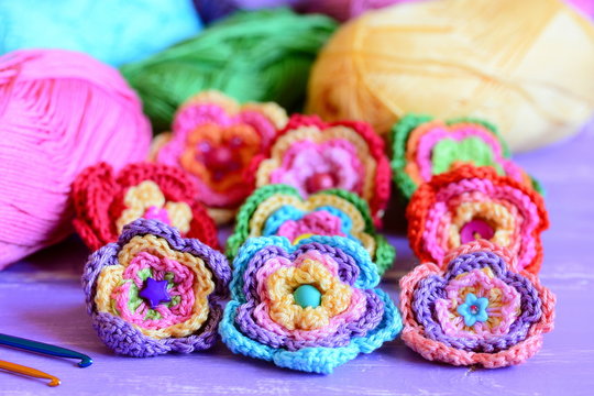 Colorful crochet flowers collection. Crochet flowers, multicolored cotton yarn, crochet hooks on purple wooden table. Easy summer handmade crafts idea. Closeup