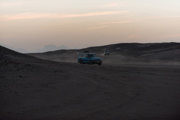 Fototapeta na wymiar White jeep cars driving on desert surface in sand dune