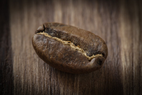 One roasted cofee bean isolated on wooden background