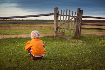 Little child sitting and waiting someone near old gates. The storm approaching