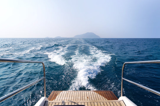 Trace of a wave with foam on the sea behind the boat. Wooden platform and metal handrails on a boat for diving.