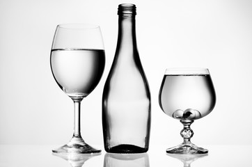 Transparent wine glasses with water near empty bottle on a white background