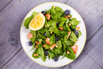 Spinach, salmon, blueberries and walnuts salad on white plate. View from above, top studio shot