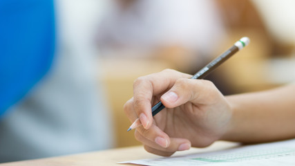 students hand holding pencil fill in Exam carbon paper sheet or test paper on wood desk
