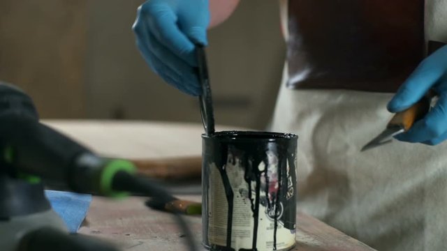 Carpenter in gloves opens a can with a dye on the workshop's table slow motion