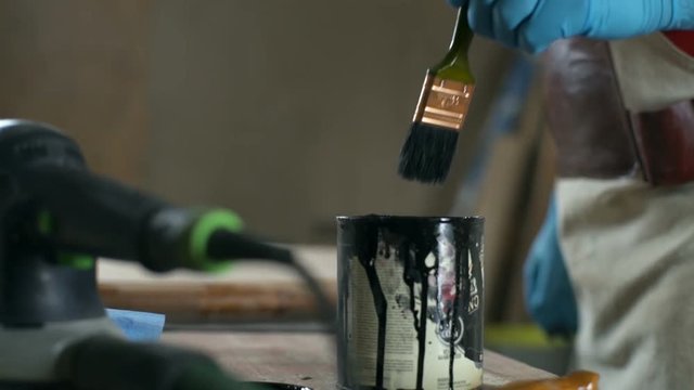 Carpenter in latex gloves dips a paintbrush into the can with black dye closeup
