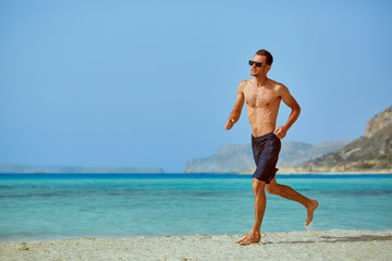 strong athletic man with bared torso running on the beach along the sea front