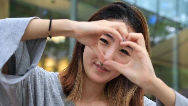 Beautiful Asian young woman making love heart gesture with hands with smile 