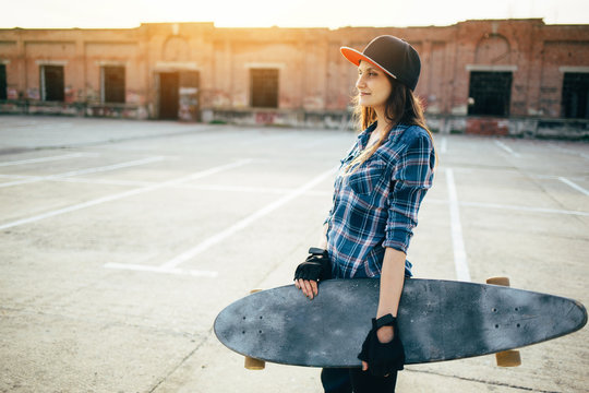 Skater girl holding longboard on sunset