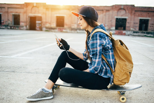 Skateboard girl listening to music with smartphone while sitting on longboard