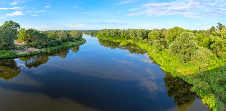Panorama of river valley with trees and bush growth on riverside reflecting in calm water. Berezichi, Kaluzhskaya region, Russia.
