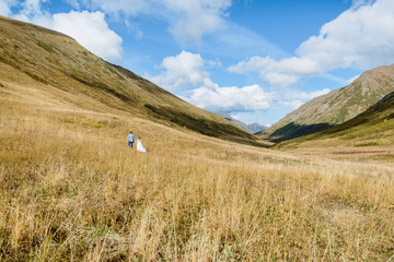 Fototapeta premium Wedding day. The groom and the bride in white dress walking in the mountains.