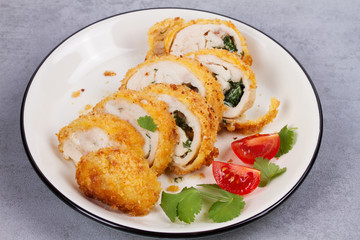 Chicken Kiev garnished with cilantro and tomatoes. Breaded chicken breast stuffed with herbs and butter on white plate
