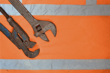 Adjustable and pipe wrenches against the background of an orange signal worker shirt