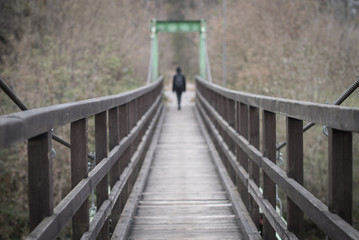 Diminishing perspective with a suspension bridge and a woman disapearing in the distance. Selective focus.