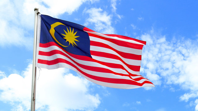 Malaysian national flag on a pole against bright blue sky.