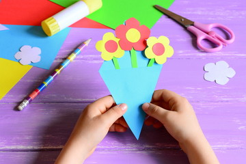 Little child made paper crafts for mother's day or birthday. Child holds a paper bouquet in hands....