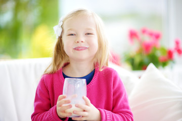 Cute little girl drinking fresh organic milk at sunny summer day. Healthy nutrition for children.