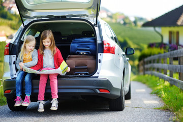 Two adorable little girls ready to go on vacations with their parents. Kids sitting in a car examining a map.