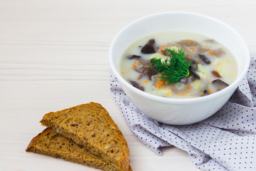 Mushroom cream soup with chopped dill and whole grain bread on wooden table