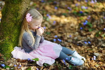 Adorable little girl picking the first flowers of spring in the woods on beautiful sunny spring day