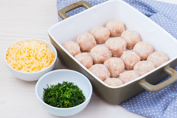 Raw chicken meatballs in ceramic backing dish. Cheese and chopped dill.