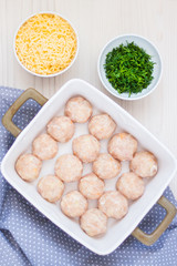 Raw chicken meatballs in ceramic backing dish. Cheese and chopped dill.