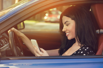 Smiling woman sending a text while driving