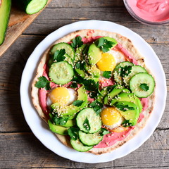 Hearty tortilla with fried quail eggs, avocado, cucumber, beet hummus and fresh parsley. Quick and healthy breakfast tortilla on a plate and on rustic wooden table. Diet food idea. Top view
