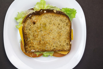 Toasted bread sandwich with lettuce, tomato and cheese overhead photo on white plate