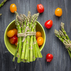 Fresh green asparagus and red and yellow tomatoes on wooden background
