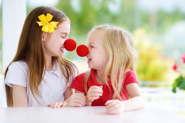 Happy little sisters wearing red clown noses having fun together on sunny summer day at home