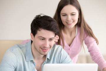 Fototapeta premium Happy lady and guy sitting together, looking at laptop screen, smiling couple searching idea for trip or vacation, making pleasant video call, shopping online, planning family home budget or wedding